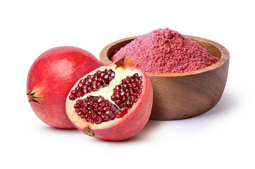 Stock photo showing a close-up, elevated view of healthy eating image of a layer of pomegranates (Punica granatum) seeds displaying red flesh (arils) encasing seeds on a red background.