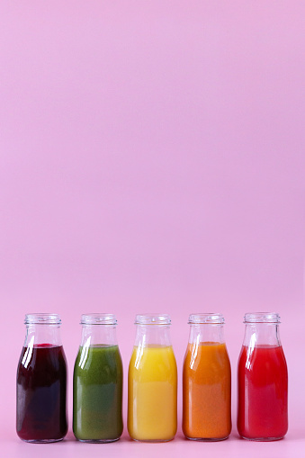 Stock photo showing close-up view of purple, green, yellow, orange and red fruit and vegetable juice smoothies in glass, screw cap bottles.