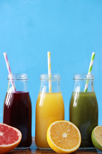 Stock photo showing close-up view of purple, yellow and green fruit and vegetable juice smoothies in glass, screw cap bottles with stripped drinking straws.