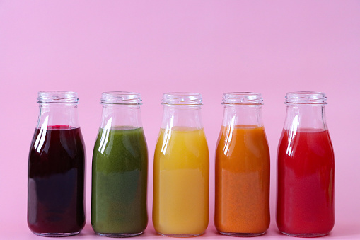Stock photo showing close-up view of purple, green, yellow, orange and red fruit and vegetable juice smoothies in glass, screw cap bottles.