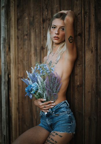 Blonde woman posing with tattoos all over her body in front of a wooden wall. Colourful and styled outfit.