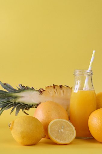 Stock photo showing close-up view of a whole and half pieces of citrus and tropical fruit including, oranges, lemon, grapefruit and pineapple besides a glass, screw cap bottle of fruit juice.