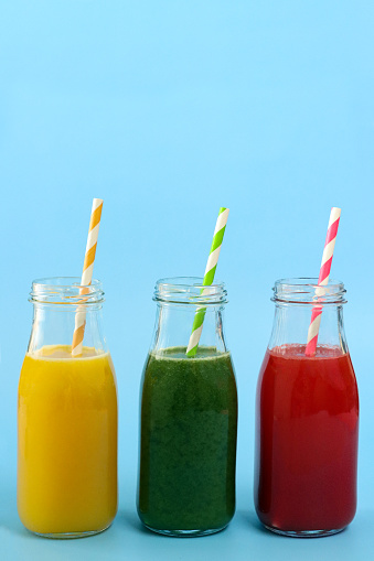 Stock photo showing close-up view of orange, green and red fruit and vegetable juice smoothies in glass, screw cap bottles with stripped drinking straw.