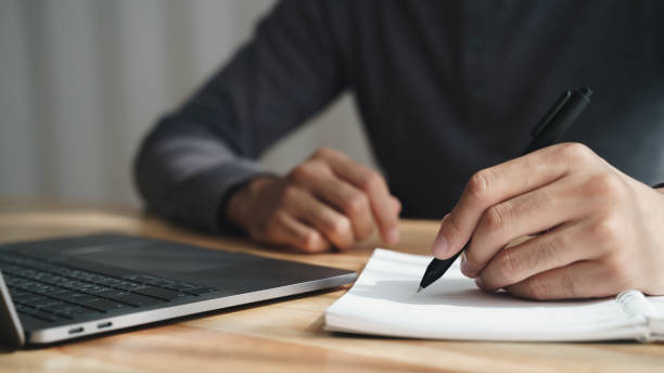 istock left handed man writes in a notebook on the table with laptop computer 1414022112