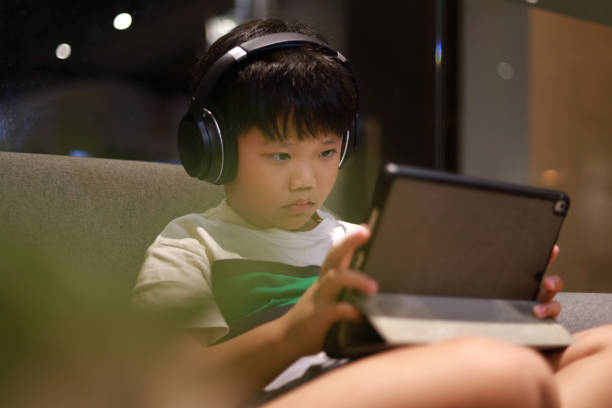 istock Boy wearing headphones and using digital tablet playing online games 1414022854