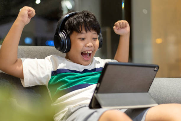 istock Boy wearing headphones and using digital tablet playing online games 1414022858