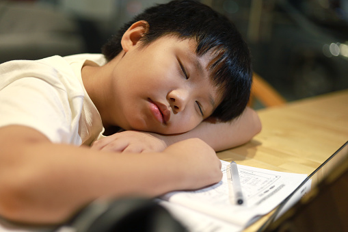 Portrait of an Asian boy in front of a digital tablet falling in sleep, he is bored and tired during online learning class