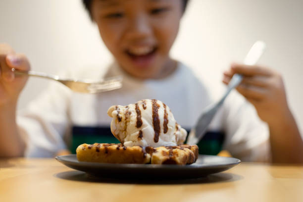 Cropped shot of a happy young Asian boy sitting alone and having waffles with ice-cream