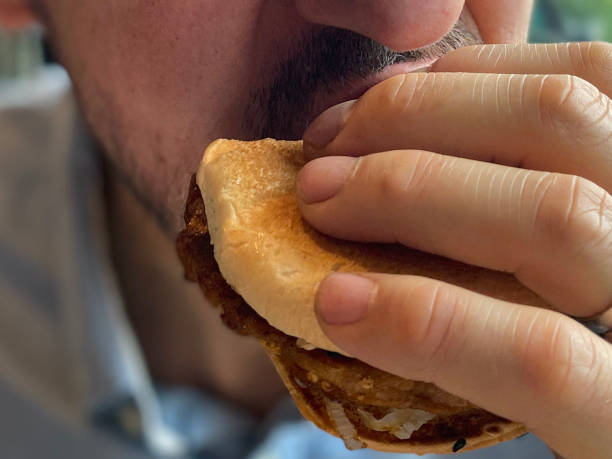 istock Full frame image of caucasian man biting into burger in a bun, focus on foreground 1414023040