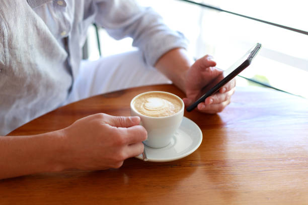 istock Casual business man, freelancer, using mobile smart phone, drinking coffee, at home office with morning sunlight, closeup 1414023820