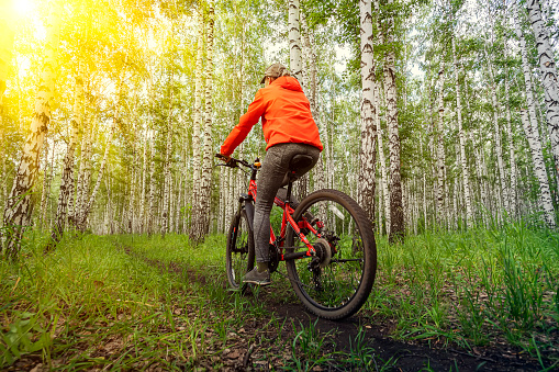Woman in a bright orange jacket riding bike on mountain top forest trail