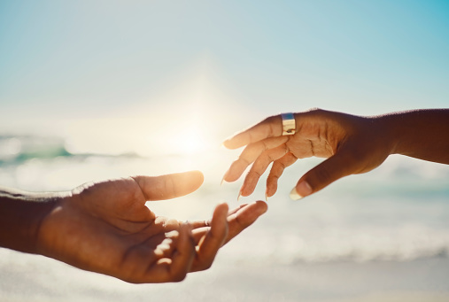 Love and care hand gesture with couple reaching for a gentle touch on blue sky and beach background with copy space. Two in love hands almost touching together as symbol or sign of romance and unity