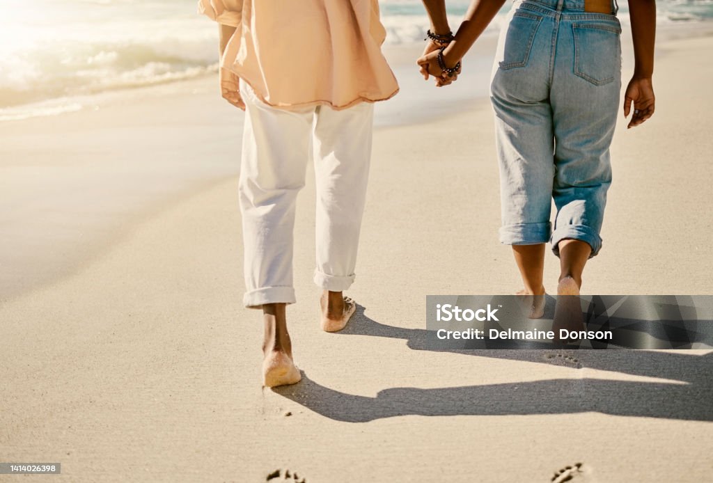 Closeup couple walking barefoot on a sandy beach and enjoying fresh air together on vacation. Low view of husband and wife taking a slow, romantic walk while holding hands while on summer holiday Couple - Relationship Stock Photo