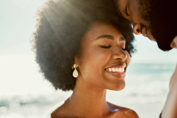 istock Young happy black couple smiling, bonding and showing affection standing on beach together on the weekend. Smiling husband and wife embracing, enjoying a romantic getaway and relaxing on honeymoon 1414026455