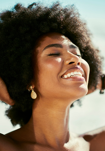Head of happy, relaxed and carefree woman enjoying the sunshine on her face while standing outside in the nude. Beautiful, sexy and attractive african female with afro smiling and being cheerful