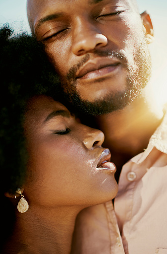 Closeup of a trendy black couple hugging and holding each other, sharing intimate moment while enjoying free time outdoors together. African American lovers closing eyes, showing affection and power