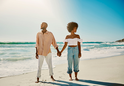 Trendy, proud and carefree black couple holding hands while enjoying walk at the beach on a sunny day. African American lovers standing in power, looking confident while bonding and relaxing together