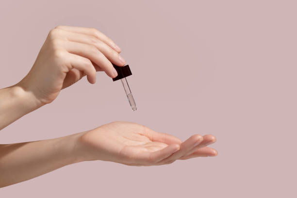 Woman hand holding facial essential oil or serum packaging on pink background. Beauty cosmetic product for skincare concept. Mockup. stock photo