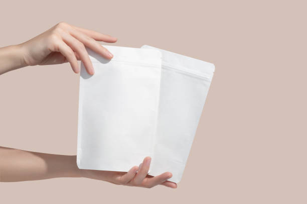 женские руки держат картонные пакеты для чая или закусок на бежевом фоне. макет чайного брендинга и упаковки. - pouch стоковые фото и изображения
