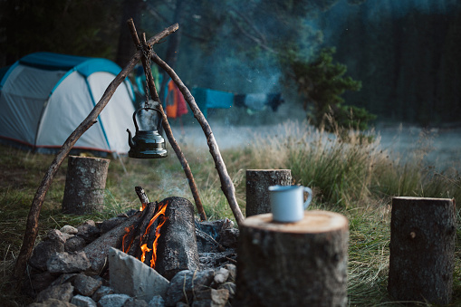 Kettle with boiling tea over open campfire on camping in the mountains.