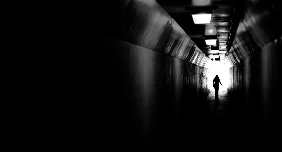 Person walking through a tunnel towards light at end. Accomplishing goal or leaving darkness.