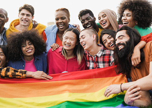 Group of happy diverse people having fun outdoor with LGBT rianbow flag - Focus on bald girl