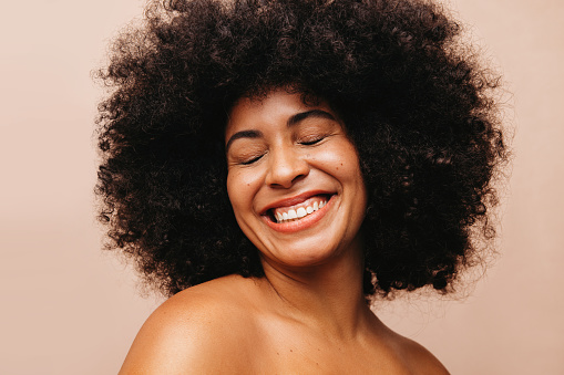 Attractive woman with an Afro hairstyle smiling cheerfully with her eyes closed. Gorgeous young woman of color wearing her natural curly hair with pride.