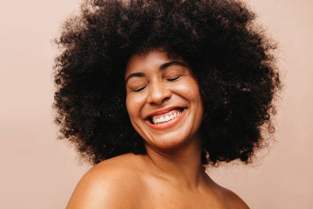 Attractive woman with Afro hair smiling happily in a studio Attractive woman with an Afro hairstyle smiling cheerfully with her eyes closed. Gorgeous young woman of color wearing her natural curly hair with pride. black hair stock pictures, royalty-free photos & images