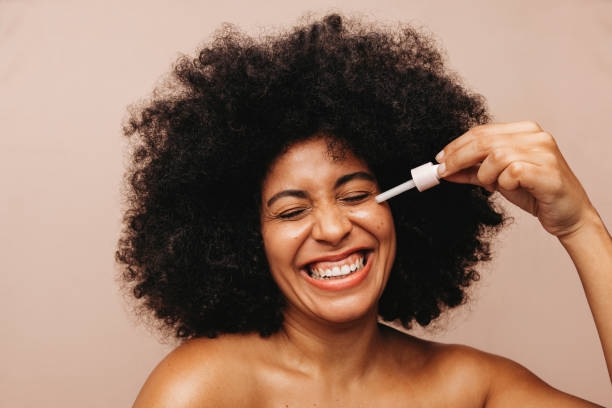 beautiful young woman applying cosmetic oil on her face - african ethnicity beauty curly hair confidence imagens e fotografias de stock