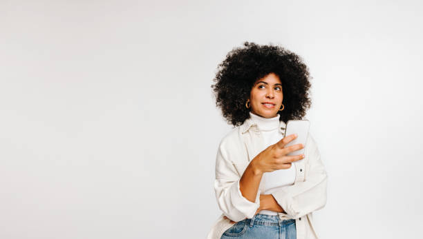 Pensive woman holding a smartphone in a studio