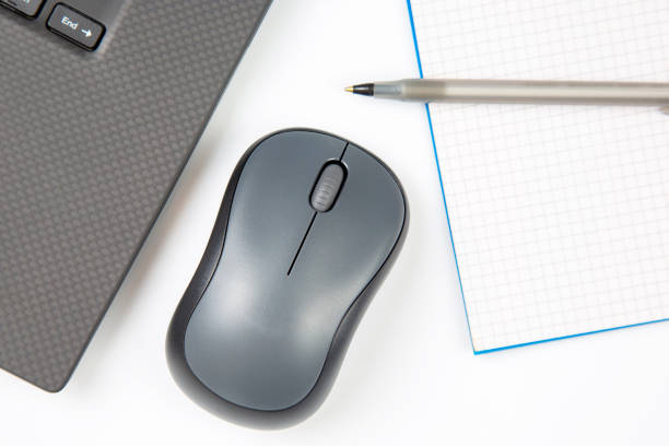istock Computer wireless mouse, pen and notepad next to a laptop on a white table close-up. Items for office work 1414034593