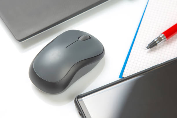 istock Computer wireless mouse, pen and notepad next to a laptop on a white table close-up. Items for office work 1414034664