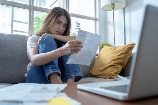 Young Asian woman stressed when she saw the expenses on her bill, Financial problems, Indebtedness, Lose a job.