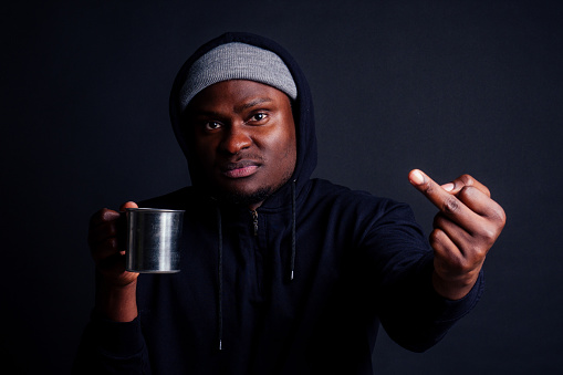 sad look african american man holding metal tourist thermos cup bad feeling.tourist alcoholic wearing gray hat and black hoody studio black background showing fuck you at camera.