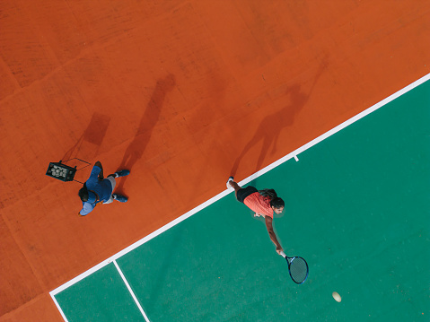 Drone point of view sport training Asian Indian female Tennis Player Serving The Ball practicing at tennis court directly above with coach guidance