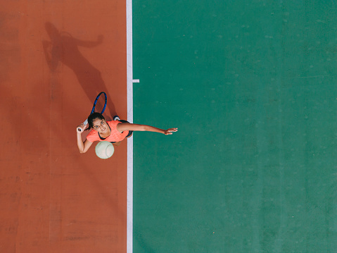 Drone point of view Asian Indian Female Tennis Player Serving The Ball practicing at tennis court directly above