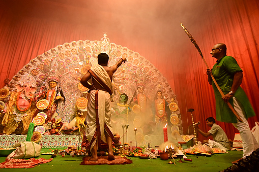 Howrah, India -October 13, 2021 : Hindu Priests worshipping Goddess Durga with hand fan. Ashtami puja aarati - sacred Durga Puja ritual - shot at night.
