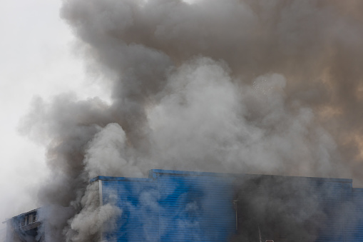 Warehouse in dense gray smoke from a strong fire. Clouds of smoke rise from the roof