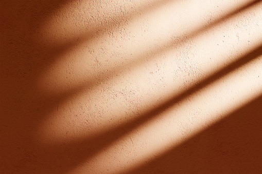 Orange concrete facade with sunlight shadow background. Indoor shade from window light on texture pastel wall.