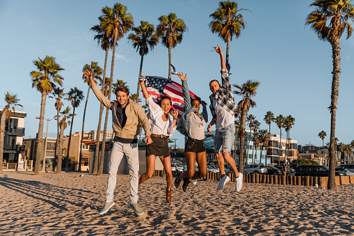 Group of happy friends jumping holding an american flag in Venice Beach, CA.