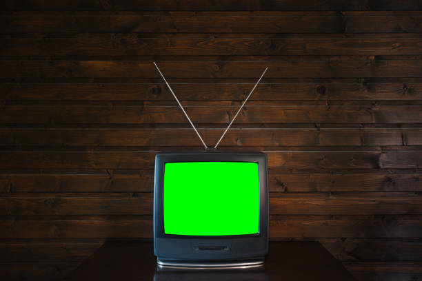Old analoque retro tv with isolate green screen mock up on dark brown wooden background in room on table. 90's style