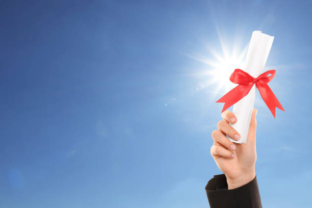 istock Graduated student holding diploma against blue sky on sunny day, closeup 1414040064