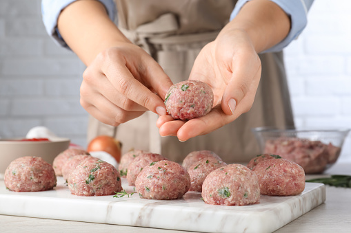 Woman making fresh raw meatballs at white table indoors, closeup