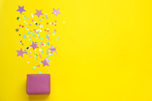 istock Different shiny confetti and box on yellow background, flat lay. Space for text 1414040327