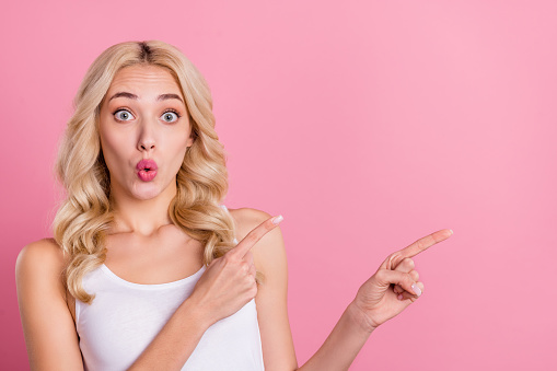 Portrait of attractive cheerful blond girl demonstrating copy space ad look isolated over pink pastel color background.