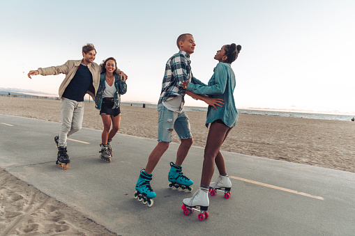 Group of four friends with roller skate in Venice Beach promenade heading to Santa Monica