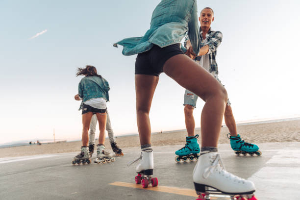 Friends roller skating by the beach in California Group of four friends with roller skate in Venice Beach promenade heading to Santa Monica inline skating stock pictures, royalty-free photos & images