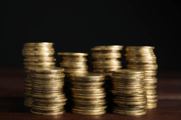 Many coins stacked on wooden table against black background