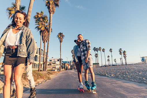 Group of four friends with roller skate in Venice Beach promenade heading to Santa Monica