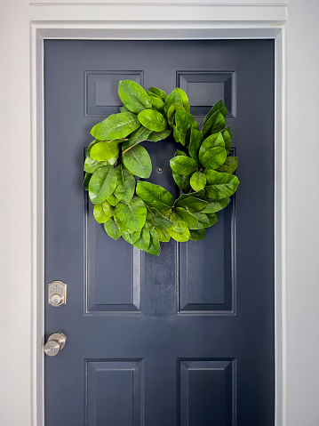 Front view of a navy blue door with a colorful green wreath on a bright, sunny day